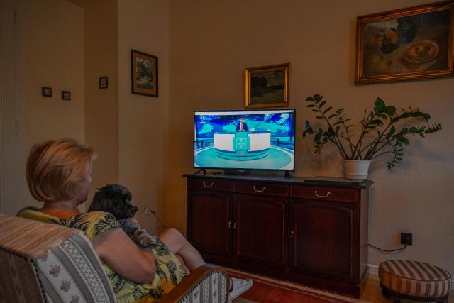 A woman sits with a dog on an armchair to watch on the TV the new news service of the relaunched state-run TV channel 1 on August 20, 2026, in Budapest, Hungary, after the news service resumed following a 44-day forced break. (Photo by Attila KISBENEDEK / AFP)