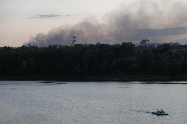 People steer a catamaran along the Dnipro River as smoke from a fire following a Russian air strike rises in the background in Kyiv on August 20, 2026, amid the Russian invasion of Ukraine. (Photo by Genya SAVILOV / AFP)