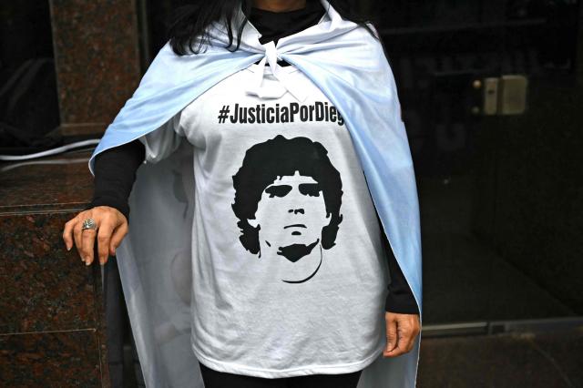 (FILES) A fan of Argentine football legend Diego Maradona wears a T-shirt depicting him as she stands outside the court before a trial hearing on his death in San Isidro, Buenos Aires province, Argentina on June 9, 2026. The trial over the death of football legend Diego Maradona has been postponed for a week, until August 27, to verify whether incorrect medical tests were used in the expert reports, the court announced on August 20, 2026. (Photo by Luis ROBAYO / AFP)