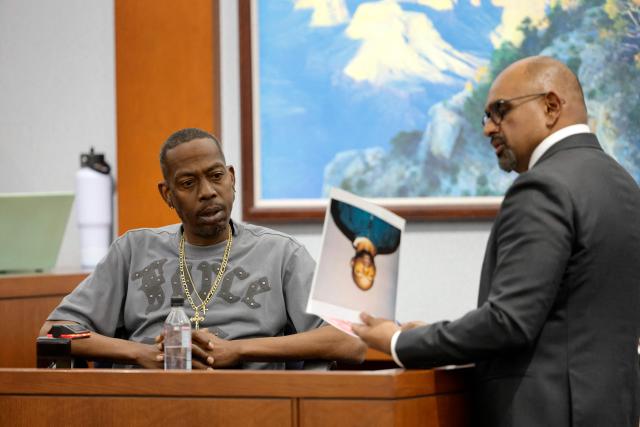 Chief Deputy District Attorney Binu Palal (R) shows pictures to Denvonta Lee, an affiliate of the gang alliance South Side Compton Crips, as he testifies during Duane Davis's murder trial, related to the 1996 killing of rapper Tupac Shakur, at Clark County District Court at the Regional Justice Center in Las Vegas, Nevada, on August 20, 2026. The trial of the former gang leader accused of orchestrating the murder of rapper Tupac Shakur began on August 10, 30 years after one of America's most high-profile unresolved killings. The proceedings, expected to last a month, will likely not make clear who fired the shots that killed the California hip-hop legend on the night of September 7, 1996, while he was in Las Vegas to see a Mike Tyson boxing match. (Photo by Steve Marcus / POOL / AFP)