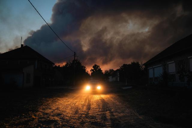 A car drives through the village of Grebenac as thick smoke from a wildfire engulfs the sky over Deliblatska Pescara (Deliblato Sands), some 70 kilometres northeast of Belgrade on August 20, 2026. Firefighters were battling wildfires across the Balkans as days of high temperatures and drought conditions continue to drive blazes in several countries, including Serbia. Scientists have long warned that climate change caused by human use of fossil fuels will make periods of drought more intense and longer-lasting, creating the ideal conditions for wildfires. (Photo by Uros Arsic / AFP)