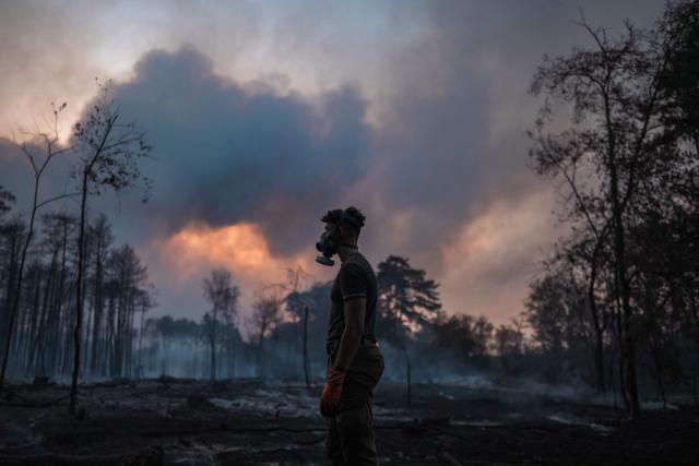 A local resident wearing a protective face mask stands in front of a scorched forest as a wildfire continues to burn in Deliblatska Pescara (Deliblato Sands), near the village of Grebenac, some 70 kilometres northeast of Belgrade on August 20, 2026. Firefighters were battling wildfires across the Balkans as days of high temperatures and drought conditions continue to drive blazes in several countries, including Serbia. Scientists have long warned that climate change caused by human use of fossil fuels will make periods of drought more intense and longer-lasting, creating the ideal conditions for wildfires. (Photo by Uros Arsic / AFP)