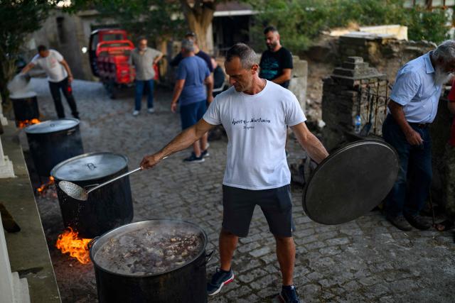 A man cooks some meat in large cauldrons for the Feast of the Dormition of the Virgin Mary near the Evangelismos Teotoku church on Gokceada (Imroz) Island, Çanakkale Province of Turkey, on August 14, 2026. Hundreds of Greeks return from Athens and around the world to Imbros each August 15 to celebrate the Virgin Mary. Like Istanbul and nearby Tenedos, the island was exempt from the 1923 population exchange between Greece and Turkey, which displaced more than 1.5 million people. (Photo by Yasin AKGUL / AFP)