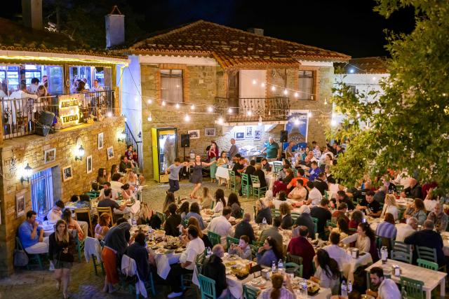 People sit at a restaurany and perform traditional Greek dance during the Feast of the Dormition of the Virgin Mary, on Gokceada (Imroz) Island, Çanakkale Province of Turkey, on August 14, 2026. Hundreds of Greeks return from Athens and around the world to Imbros each August 15 to celebrate the Virgin Mary. Like Istanbul and nearby Tenedos, the island was exempt from the 1923 population exchange between Greece and Turkey, which displaced more than 1.5 million people. (Photo by Yasin AKGUL / AFP)