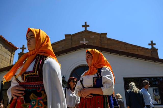 Young women in traditional cloths walk in front of the Evangelismos Teotoku Church during the Feast of the Dormition of the Virgin Mary, on Gokceada (Imroz) Island, Çanakkale Province of Turkey, on August 15, 2026. Hundreds of Greeks return from Athens and around the world to Imbros each August 15 to celebrate the Virgin Mary. Like Istanbul and nearby Tenedos, the island was exempt from the 1923 population exchange between Greece and Turkey, which displaced more than 1.5 million people. (Photo by Yasin AKGUL / AFP)