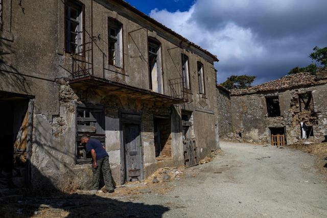 Local resident Yorgi Baki looks through a window of an abandoned house in Derekoy village, where mostly abandoned by the Greek residents after clashes with the Turkish community in the 1960's, on Gokceada (Imroz) Island, Çanakkale Province of Turkey, on August 16, 2026. Hundreds of Greeks return from Athens and around the world to Imbros each August 15 to celebrate the Virgin Mary. Like Istanbul and nearby Tenedos, the island was exempt from the 1923 population exchange between Greece and Turkey, which displaced more than 1.5 million people. (Photo by Yasin AKGUL / AFP)