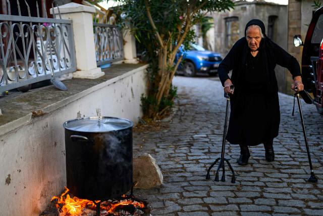 Vasiliki kamburopulu passes by a cauldron simmering over a fire the Feast of the Dormition of the Virgin Mary, on Gokceada (Imroz) Island, Canakkale Province of Turkey, on August 15, 2026. Hundreds of Greeks return from Athens and around the world to Imbros each August 15 to celebrate the Virgin Mary. Like Istanbul and nearby Tenedos, the island was exempt from the 1923 population exchange between Greece and Turkey, which displaced more than 1.5 million people. (Photo by Yasin AKGUL / AFP)