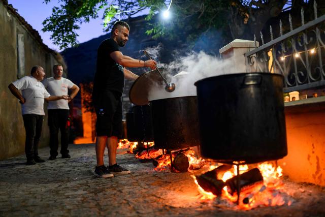 A man cooks some meat in large cauldrons for the Feast of the Dormition of the Virgin Mary near the Evangelismos Teotoku church on Gokceada (Imroz) Island, Çanakkale Province of Turkey, on August 14, 2026. Hundreds of Greeks return from Athens and around the world to Imbros each August 15 to celebrate the Virgin Mary. Like Istanbul and nearby Tenedos, the island was exempt from the 1923 population exchange between Greece and Turkey, which displaced more than 1.5 million people. (Photo by Yasin AKGUL / AFP)