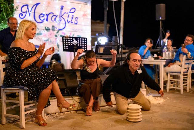 Konstantin Kostanoglu (R) and Tuba Demir (C) perform at a tavern during the Feast of the Dormition of the Virgin Mary, on Gokceada (Imroz) Island, Çanakkale Province of Turkey, on August 14, 2026. Hundreds of Greeks return from Athens and around the world to Imbros each August 15 to celebrate the Virgin Mary. Like Istanbul and nearby Tenedos, the island was exempt from the 1923 population exchange between Greece and Turkey, which displaced more than 1.5 million people. (Photo by Yasin AKGUL / AFP)