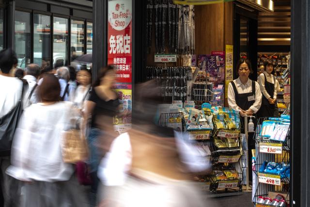 Staff members of a tax free shop watch as pedestrians walk past at the Ginza shopping district in Tokyo on August 21, 2026. (Photo by Philip FONG / AFP)