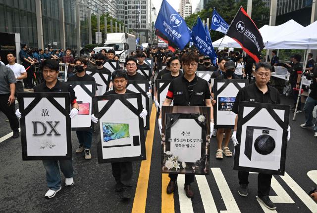 Members of the Samsung Electronics Company Union carry placards featuring company products during a rally demanding compensation negotiations in front of the Samsung Electronics Seocho building in Seoul on August 21, 2026. (Photo by Jung Yeon-je / AFP)
