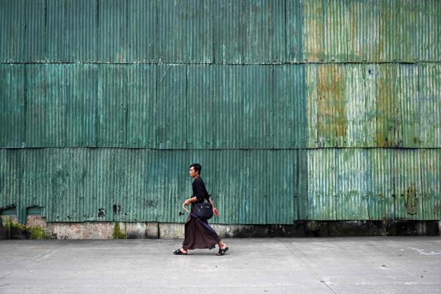 A man walks past a large green corrugated iron warehouse wall in Yangon on August 21, 2026. (Photo by SAI AUNG MAIN / AFP)