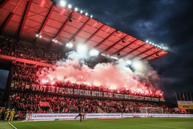 Standard's supporters light flares with a banner reading "so many ways to describe our name, all recall our history" with a placard reading "pyrotechnics are banned in the stadium" during the Belgian "Pro League" First Division football match between Standard Liege and RAAL La Louviere at Stade Maurice Dufrasne in Liege on Augst 21, 2026. (Photo by BRUNO FAHY / BELGA / AFP) / Belgium OUT