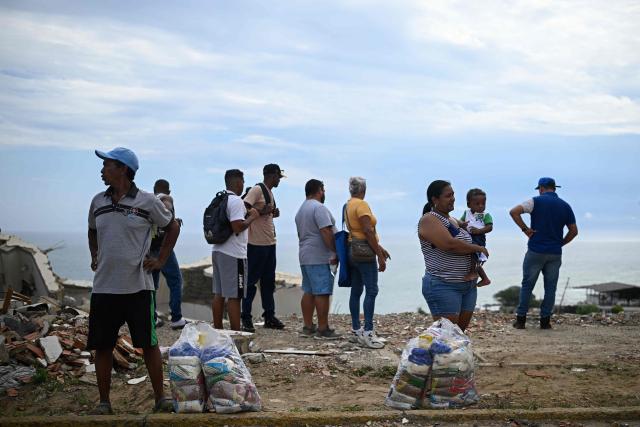Residents stand next to food packages distributed by the World Food Programme (WFP) near collapsed buildings in Catia La Mar, La Guaira state, Venezuela, on August 21, 2026, two months after earthquakes of magnitudes 7.2 and 7.5 struck the area. (Photo by Federico PARRA / AFP)