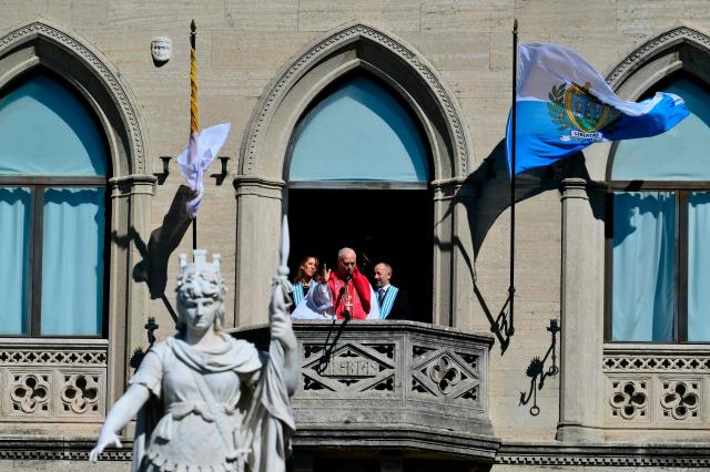 Pope Leo XIV, flanked by San Marino's Captains Regent Alice Mina and Vladimiro Selva, greets the crowd from the balcony of the Public Palace during a pastoral visit to San Marino on August 22, 2026. (Photo by Stefano RELLANDINI / AFP)