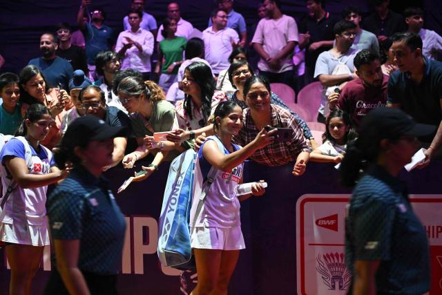 India's Treesa Jolly (front L) and Gayatri Gopichand Pullela (front C) take photos with fans at the end of their BWF World Championships women's doubles semi-final badminton match against China's Liu Sheng Shu and Tan Ning at the Indira Gandhi Indoor Stadium in New Delhi on August 22, 2026. (Photo by Arun SANKAR / AFP)