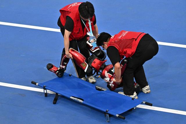 Staff members pick up a humanoid robot that fell while competing on the first day of the 2nd World Humanoid Robot Games in Beijing on August 22, 2026. (Photo by Pedro PARDO / AFP)