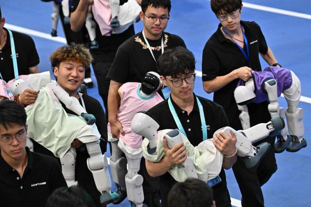 Staff members collect humanoid robots after the opening ceremony of the 2nd World Humanoid Robot Games in Beijing on August 22, 2026. (Photo by Pedro PARDO / AFP)