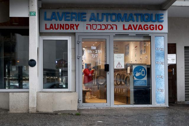 A customer stands in a laundromat with Hebrew script on its storefront on a street of the French high-altitude resort of Les Deux Alpes, south-eastern France, on August 19, 2026. For decades, Orthodox Jewish communities have been gathering in the open air in the tranquillity of the Alps during the summer. However, their presence and their highly regimented way of life sometimes cause tension, or even rejection, amongst locals and other holidaymakers. In mid-August, a video filmed at the Deux Alpes resort in the Isиre department, on the edge of the Йcrins massif, went viral on X. It shows a shopkeeper leaning against the counter of her refreshment bar saying to an Orthodox Jewish man: "The Jewish community – there are too many of you. At some point, it gets on people’s nerves." (Photo by Alex MARTIN / AFP)