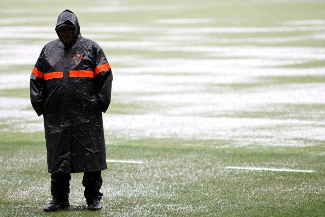 A football steward stands on the pitch of the Akron stadium as rain falls delaying the Liga MX Apertura football match between Guadalajara and Tijuana in Zapopan, Jalisco, Mexico on August 22, 2026. (Photo by ULISES RUIZ / AFP)