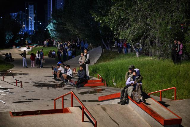 People sit in a skate park as they watch a concert from outside the closed perimeter of the show in Ulaanbaatar early on August 23, 2026. (Photo by Hector RETAMAL / AFP)