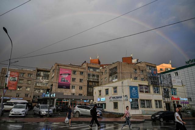 People walk on a street under a rainbow arc in Ulaanbaatar on August 22, 2026. (Photo by Hector RETAMAL / AFP)