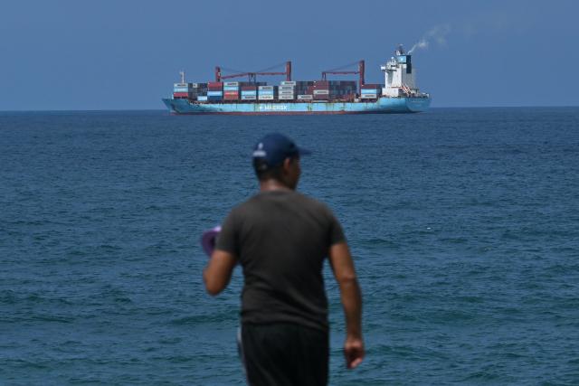 A cargo ship sails as a man stands on the coastline at La Guaira Port, Venezuela on August 22, 2026. The Venezuelan Parliament announced an investigation into opposition lawmaker Antonio Ecarri on August 22, 2026, and removed him from his legislative post after he proposed dollarizing the economy with the advice of US economist Steve Hanke. (Photo by Juan BARRETO / AFP)