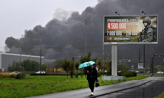 Smoke rises over a logistics center in Kolpino, outside Saint Petersburg in front of a billboard promoting contract army service after being hit by Ukrainian drones early on August 23, 2026. (Photo by AFP)