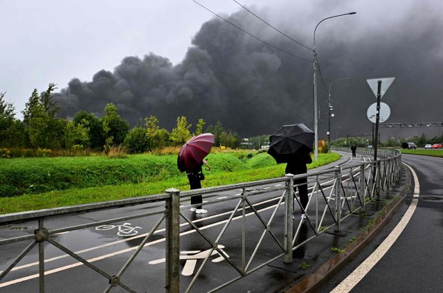 People watvh the smoke rising over a logistics center in Kolpino, outside Saint Petersburg after being hit by Ukrainian drones early on August 23, 2026. (Photo by AFP)
