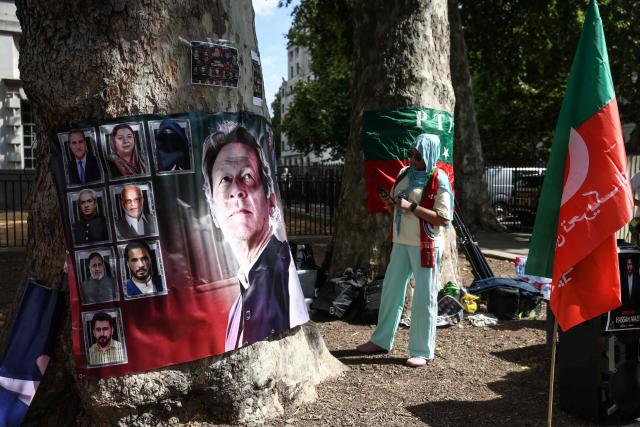 A woman looks at a banner showing Pakistan's jailed former prime minister Imran Khan (L) as a small group of people hold a rally opposite Downing Street in central London on August 23, 2026. The ex-cricket captain, who was prime minister from 2018 to 2022, was sentenced along with his wife in late 2025 to 17 years in prison in a case Khan argues was politically motivated. (Photo by Toby Shepheard / AFP)