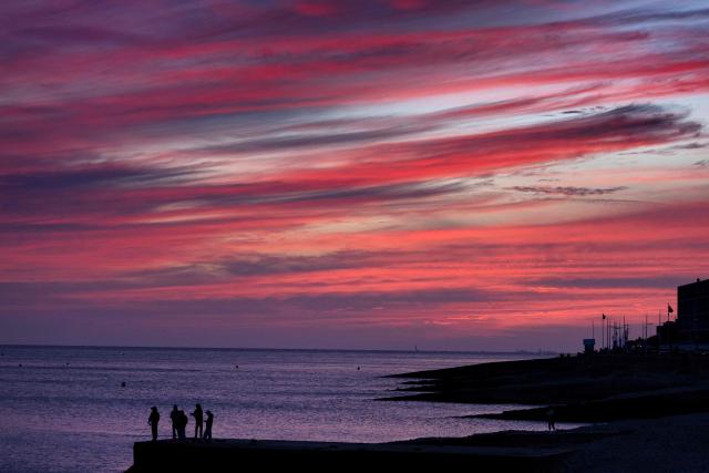 People stand on the jetty as they fish at sunset, in Le Havre, northwestern France on August 23, 2026. (Photo by Fred TANNEAU / AFP)