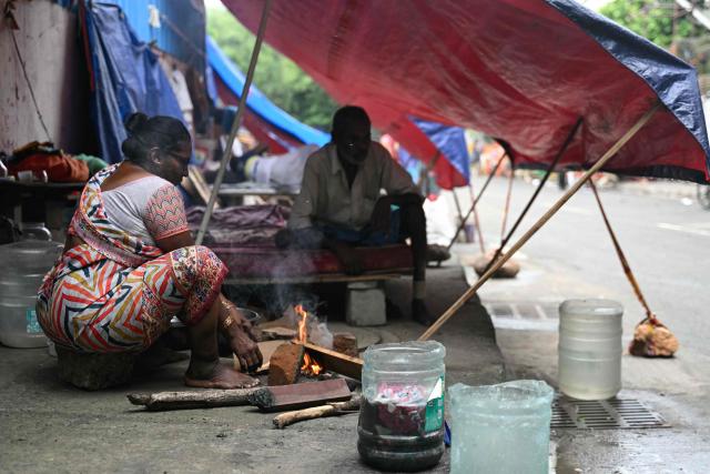 A woman prepares to cook inside her tent, along a roadside in Chennai on August 24, 2026. (Photo by R. Satish BABU / AFP)