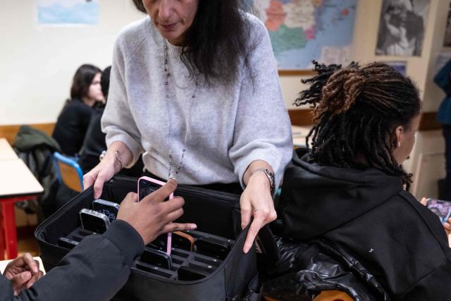 (FILES) A teacher collects a student's mobile phone, set aside during classes at the Jean Mermoz vocational high school in Montsoult, in the northern suburbs of Paris, on January 14, 2026. The ban on mobile phones in high schools "could take effect as early as the start of the school year" next week, government spokesperson Maud Bregeon announced on August 24, 2026. (Photo by BERTRAND GUAY / AFP)