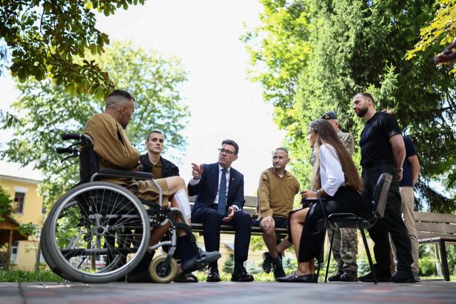 Britain's prime minister Andy Burnham (C) gestures as he meets patients wounded in the war at the Main Military Hospital, supported by the David Nott Foundation, a UK charity who have trained over 1,000 Ukrainian surgeons, anaesthetists and other healthcare workers, in Kyiv on August 24, 2026. Ukraine hosts a meeting of its key European backers on August 24 to press for critical air-defence supplies and more pressure on Moscow, with Russian attacks killing more civilians than at any time since the first months of the invasion. The leaders of Luxembourg, Moldova, Estonia and EU Council President Antonio Costa are also in Kyiv for the talks hosted on Ukraine's Independence Day and which come amid the war's latest escalation. (Photo by Henry NICHOLLS / POOL / AFP)