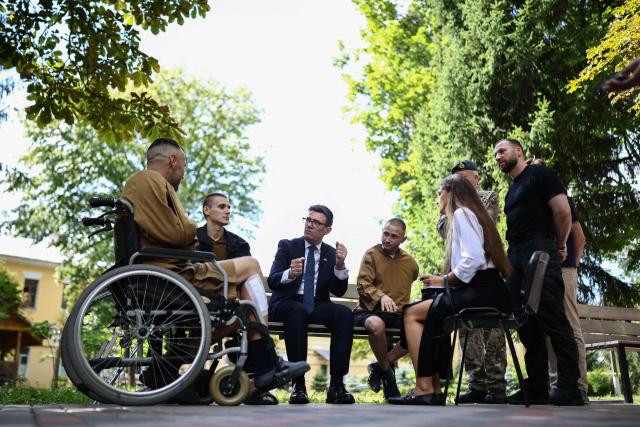 Britain's prime minister Andy Burnham (C) gestures as he meets patients wounded in the war at the Main Military Hospital, supported by the David Nott Foundation, a UK charity who have trained over 1,000 Ukrainian surgeons, anaesthetists and other healthcare workers, in Kyiv on August 24, 2026. Ukraine hosts a meeting of its key European backers on August 24 to press for critical air-defence supplies and more pressure on Moscow, with Russian attacks killing more civilians than at any time since the first months of the invasion. The leaders of Luxembourg, Moldova, Estonia and EU Council President Antonio Costa are also in Kyiv for the talks hosted on Ukraine's Independence Day and which come amid the war's latest escalation. (Photo by Henry NICHOLLS / POOL / AFP)