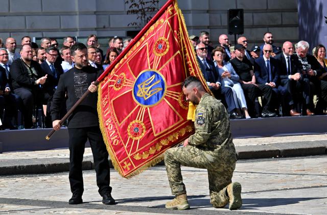 Ukraine's President Volodymyr Zelensky hands over the ceremonial battle flag with a slogan reading "For Ukraine, For its freedom" to the brigade commander during a commemorative ceremony marking Ukraine's 35th Independence Day outside St. Sofia cathedral in Kyiv on August 24, 2026. Ukraine hosts a meeting of its key European backers on August 24 to press for critical air-defence supplies and more pressure on Moscow, with Russian attacks killing more civilians than at any time since the first months of the invasion. The leaders of Luxembourg, Moldova, Estonia and EU Council President Antonio Costa are also in Kyiv for the talks hosted on Ukraine's Independence Day and which come amid the war's latest escalation. (Photo by Sergei SUPINSKY / AFP)