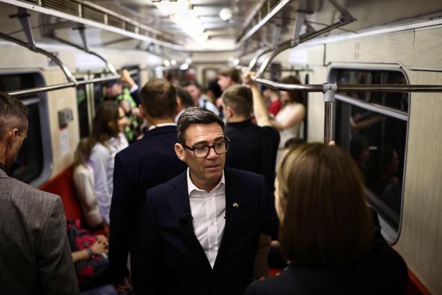 Britain's Prime Minister Andy Burnham (C) reacts as he stands in a metro carriage among passengers during the journey between the metro stations Zoloti Vorota and Lukanivska, in Kyiv, on August 24, 2026, as part of his first trip abroad since taking office. The United Kingdom will keep providing defence aid to Ukraine despite Russia's threats, Prime Minister Andy Burnham said on August 24, 2026 on a visit to Kyiv where allies gathered to discuss support. Air defence supplies are due to be the main priority at the meeting of the Coalition of the Willing, jointly chaired by the leaders of France and Germany, who will participate remotely, and by Britain's Burnham. (Photo by Henry NICHOLLS / POOL / AFP)