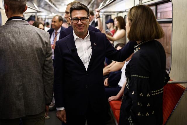 Britain's Prime Minister Andy Burnham (C) reacts as he stands in a metro carriage among passengers during the journey between the metro stations Zoloti Vorota and Lukanivska, in Kyiv, on August 24, 2026, as part of his first trip abroad since taking office. The United Kingdom will keep providing defence aid to Ukraine despite Russia's threats, Prime Minister Andy Burnham said on August 24, 2026 on a visit to Kyiv where allies gathered to discuss support. Air defence supplies are due to be the main priority at the meeting of the Coalition of the Willing, jointly chaired by the leaders of France and Germany, who will participate remotely, and by Britain's Burnham. (Photo by Henry NICHOLLS / POOL / AFP)