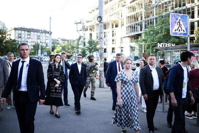 Britain's Prime Minister Andy Burnham (C) walks in the street and reacts as he is shown the rubbles and wreckages left on the buildings and site of a strike by the Lukanivska market, in Kyiv, on August 24, 2026, during his first trip abroad since taking office. The United Kingdom will keep providing defence aid to Ukraine despite Russia's threats, Prime Minister Andy Burnham said on August 24, 2026 on a visit to Kyiv where allies gathered to discuss support. Air defence supplies are due to be the main priority at the meeting of the Coalition of the Willing, jointly chaired by the leaders of France and Germany, who will participate remotely, and by Britain's Burnham. (Photo by Henry NICHOLLS / POOL / AFP)