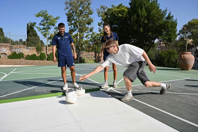 People try the winter sport of curling on ice-free synthetic curling rinks set up in Colle Oppio Park overlooking the Colosseum during a hot summer day in Rome on August 24, 2026. (Photo by Andreas SOLARO / AFP)