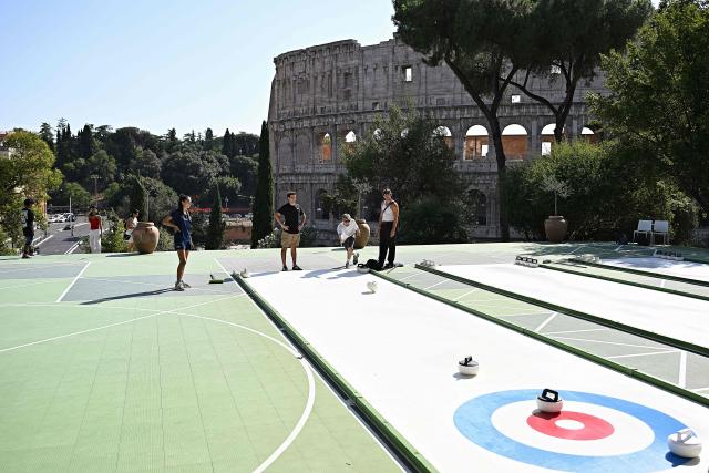 People try the winter sport of curling on ice-free synthetic curling rinks set up in Colle Oppio Park overlooking the Colosseum during a hot summer day in Rome on August 24, 2026. (Photo by Andreas SOLARO / AFP)