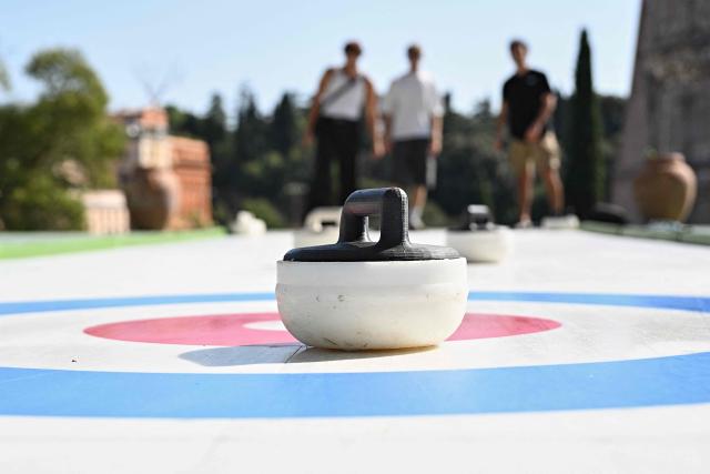 People try the winter sport of curling on ice-free synthetic curling rinks set up in Colle Oppio Park overlooking the Colosseum during a hot summer day in Rome on August 24, 2026. (Photo by Andreas SOLARO / AFP)