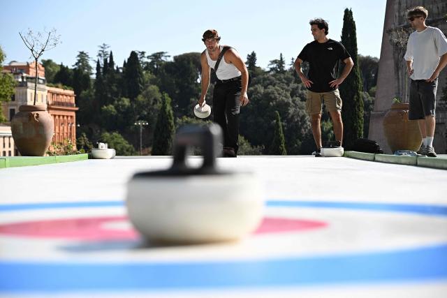 People try the winter sport of curling on ice-free synthetic curling rinks set up in Colle Oppio Park overlooking the Colosseum during a hot summer day in Rome on August 24, 2026. (Photo by Andreas SOLARO / AFP)
