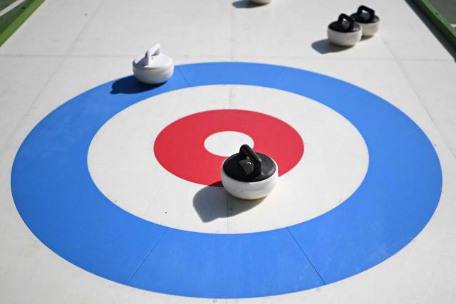 People try the winter sport of curling on ice-free synthetic curling rinks set up in Colle Oppio Park overlooking the Colosseum during a hot summer day in Rome on August 24, 2026. (Photo by Andreas SOLARO / AFP)