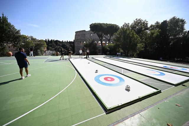 People try the winter sport of curling on ice-free synthetic curling rinks set up in Colle Oppio Park overlooking the Colosseum during a hot summer day in Rome on August 24, 2026. (Photo by Andreas SOLARO / AFP)