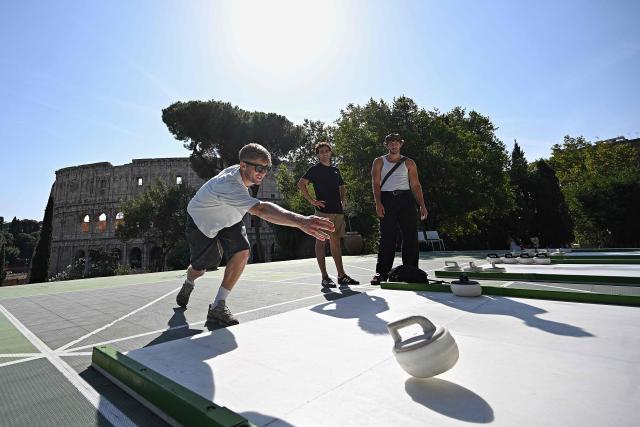 People try the winter sport of curling on ice-free synthetic curling rinks set up in Colle Oppio Park overlooking the Colosseum during a hot summer day in Rome on August 24, 2026. (Photo by Andreas SOLARO / AFP)