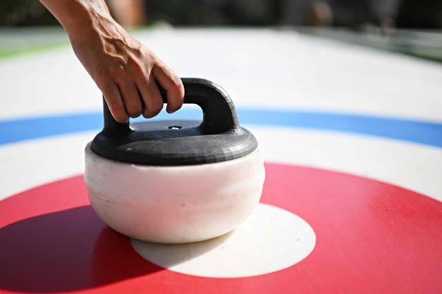 People try the winter sport of curling on ice-free synthetic curling rinks set up in Colle Oppio Park overlooking the Colosseum during a hot summer day in Rome on August 24, 2026. (Photo by Andreas SOLARO / AFP)