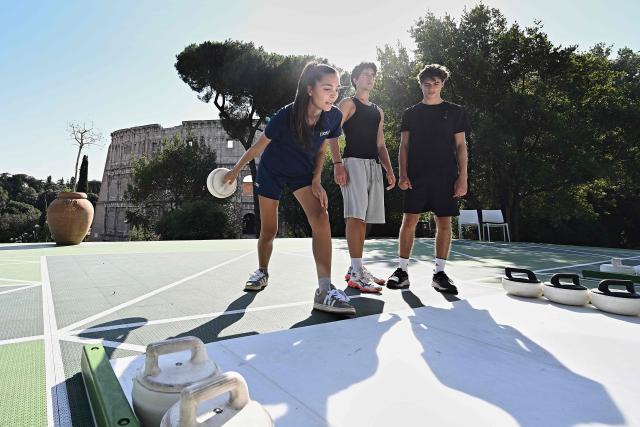 Tutor's curling Serena Rota shows how to throw the stone as people try the winter sport of curling on ice-free synthetic curling rinks set up in Colle Oppio Park overlooking the Colosseum during a hot summer day in Rome on August 24, 2026. (Photo by Andreas SOLARO / AFP)