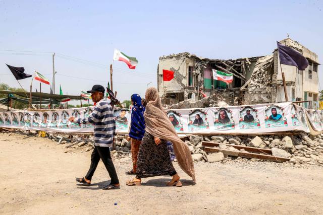 People walk near the building of the destroyed Shajareh Tayebeh primary school in Minab in Irans Hormozgan province on August 10, 2026. Six months on, a team of AFP journalists obtained rare access to the school which has remained largely in ruins, its collapsed walls and twisted steel now surrounded by portraits of the children killed as Iranian flags flutter above the rubble. Iran says the attack on the school involved two separate US Tomahawk missiles but neither the United States nor Israel has officially claimed responsibility for the strike. (Photo by ATTA KENARE / AFP) / 