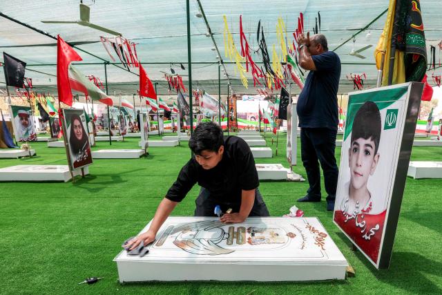 A boy cleans one of the graves of people and children killed during the strike on the Shajareh Tayebeh primary school at a cemetery in Minab in Irans Hormozgan province on August 10, 2026. Six months on, a team of AFP journalists obtained rare access to the school which has remained largely in ruins, its collapsed walls and twisted steel now surrounded by portraits of the children killed as Iranian flags flutter above the rubble. Iran says the attack on the school involved two separate US Tomahawk missiles but neither the United States nor Israel has officially claimed responsibility for the strike. (Photo by ATTA KENARE / AFP) / 